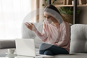 Happy young woman waving hand making video call on laptop