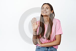 Happy young woman waving hand and smiling, looking away with friendly face, greeting someone with hello wave gesture