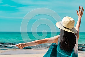 Happy young woman wear straw hat sit and raised hand at sand beach. Relaxing and enjoy holiday at tropical paradise beach