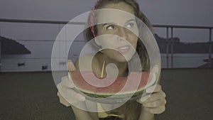 Happy young woman wearing bikini eating watermelon on the rooftop with beatiful view behind