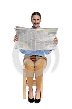 Happy young woman reading newspaper and smiling