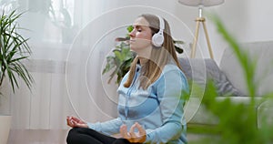 A happy young woman wearing headphones practicing yoga and meditation at home