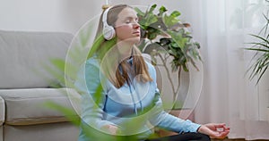 A happy young woman wearing headphones practicing yoga and meditation at home