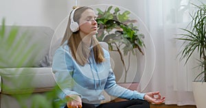 A happy young woman wearing headphones practicing yoga and meditation at home