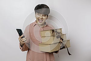 A happy young woman is wearing a pink shirt while holding a stack of presents and her smartphone