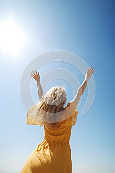 happy young woman wearing sun dress throwing hands up in the air