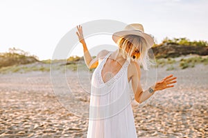 Happy young woman wearing white long dress and straw hat dance alone beach during dawn. Happiness, freedom