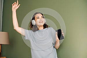 Happy young woman wearing wireless headphones listening to music, enjoying free time, dancing, having fun. Melodic