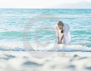 Happy young woman wetting hands in sea