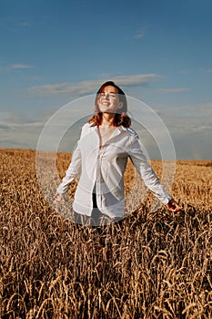 Happy young woman in a white shirt in a wheat field. Sunny day.