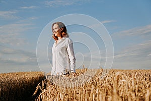 Happy young woman in a white shirt in a wheat field. Sunny day.