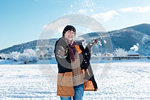 A happy young woman in winter clothes throws a snowball in a snowy park. Mountains in the background. Christmas holidays