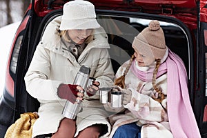 Happy young woman in winterwear pouring hot tea in metallic mugs