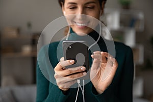 Happy young woman in wired earphones using smartphone.