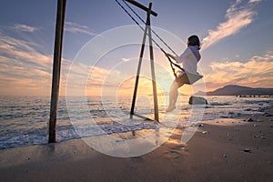 Happy young woman on wooden swing in water, sea with waves