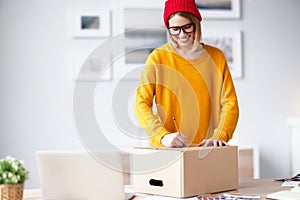 Happy young woman writing address on parcel