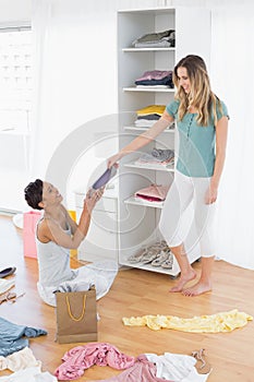 Happy young women arranging clothes in shelf