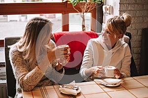 Happy young women with coffee cups at cafe, have conversation, laughing, fun moments, lifestyle