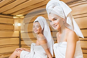 happy young women covered with towels relxing in sauna and looking