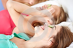 Happy young women with cucumber mask lying in bed