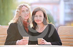 Happy young women friends drinking coffee at city street restaurant during work break. Socializing and friendship