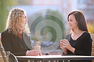 Happy young women friends drinking coffee at city street restaurant during work break. Socializing and friendship