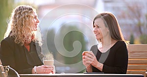 Happy young women friends drinking coffee at city street restaurant during work break. Socializing and friendship