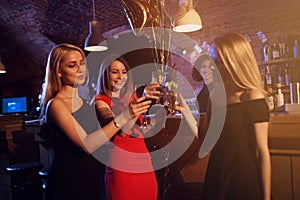 Happy young women with glasses of wine and cocktails enjoying a night out in stylish bar