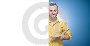 Happy young women holding white board over blue background, dresses in yellow shirt. Handsome guy showing blank empty paper