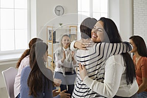 Happy young women hugging each other in support group meeting or therapy session