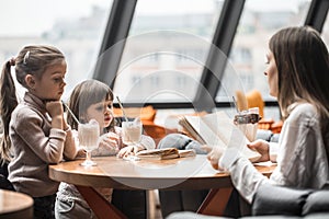 Happy young women mother with children sitting at dinner table and talking in restaurant