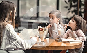 Happy young women mother with children sitting at dinner table and talking in restaurant