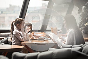 Happy young women mother with children sitting at dinner table and talking in restaurant