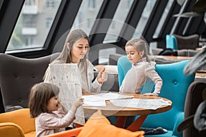 Happy young women mother with children sitting at dinner table and talking in restaurant