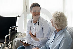 Happy young woman doctor consult disabled handicapped old grandma patient photo