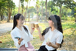 Happy young women office workers sitting on park bench and drinking coffee