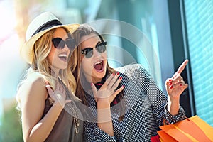 Happy young women with shopping bags pointing finger to shop window