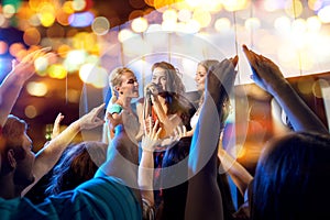 Happy young women singing karaoke in night club