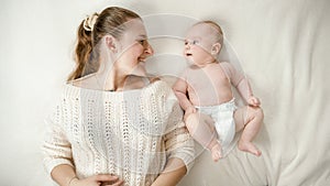 Happy young woman smiling at her little baby son on bed