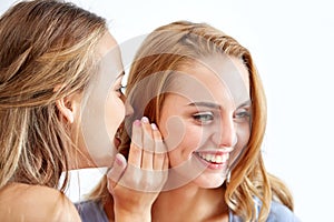 Happy young women whispering gossip at home