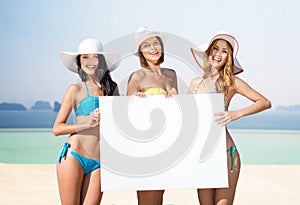 Happy young women with white board on summer beach