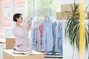 Happy young worker of online shop office photographing blue shirt on hangers