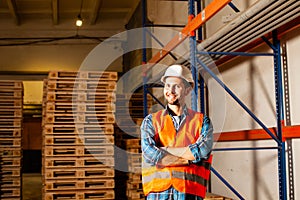 Happy young worker in protective uniform in front of wooden pallets