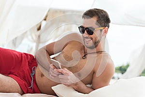 Happy youthful man with beard texting via gadget on beach