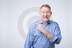 Happymature guy in blue shirt looking at camera, smiling and pointing aside