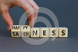Happyness or sadness symbol. Businessman turns cubes and changes the word `sadness` to `happyness`. Beautiful grey background.