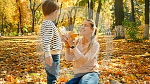 Hapyy smiling boy giving beautiful yellow and red leaves to his mother in autumn park