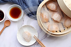 Har Gow - traditional shrimp dumpling Dim Sum in a small plate and in bamboo steamer with sauce and chopsticks