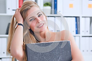 Beautiful young secretary hides her nakedness for a folder on an office background. Harassment concept.