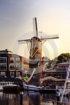 Harbor with sailing boats and an old windmill during the sunset